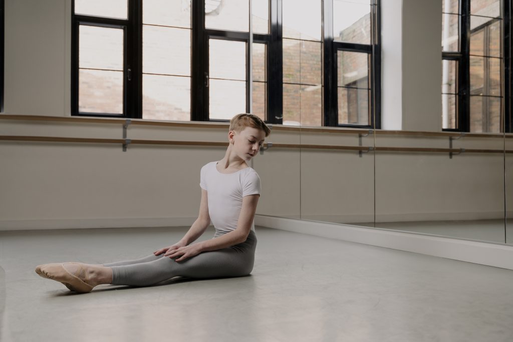 A young male dancer sat alone in a dance studio showcasing skin toned dancewear, Shades Dancewear